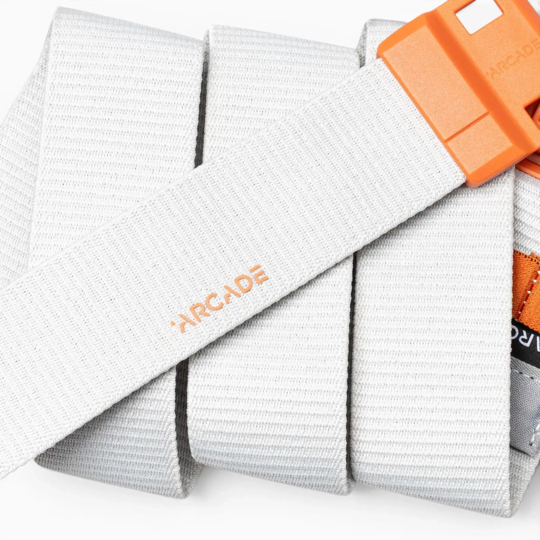 A close-up of a light gray Arcade Belts Polar Mag, a durable belt with an orange buckle, neatly rolled up. The Arcade logo is printed in orange on the belt, and it features SwiftLock technology for a secure fit.