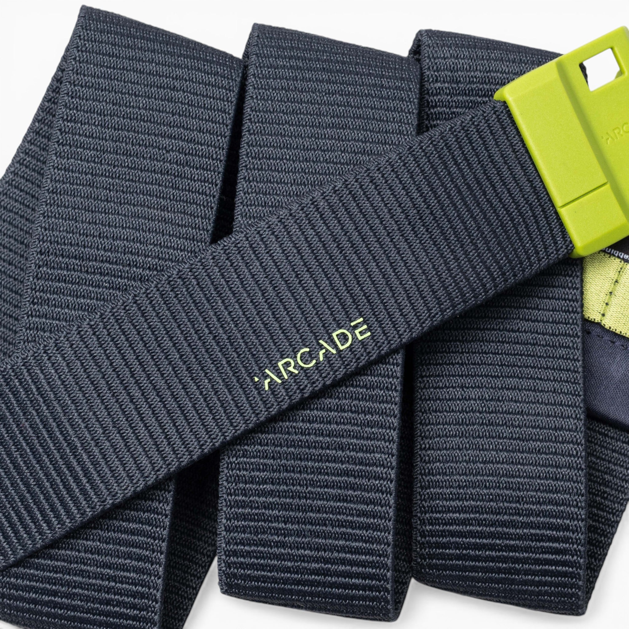 A close-up of a dark gray Arcade Belts Polar Mag durable belt with a lime green buckle, featuring SwiftLock technology, laid out in overlapping folds.