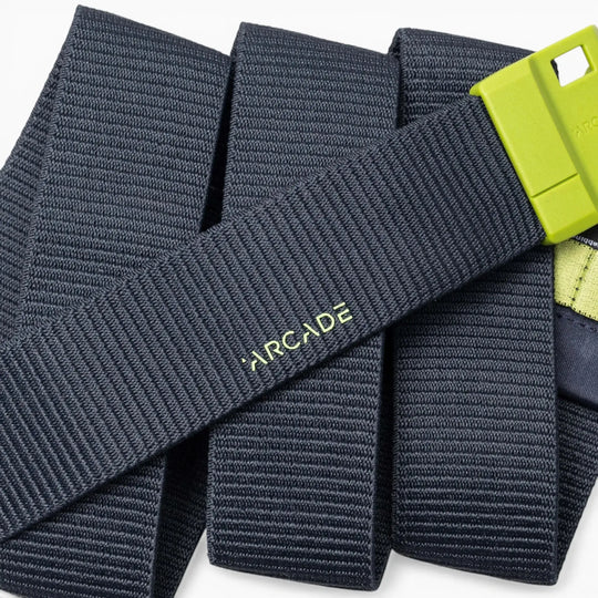 A close-up of a dark gray Arcade Belts Polar Mag durable belt with a lime green buckle, featuring SwiftLock technology, laid out in overlapping folds.