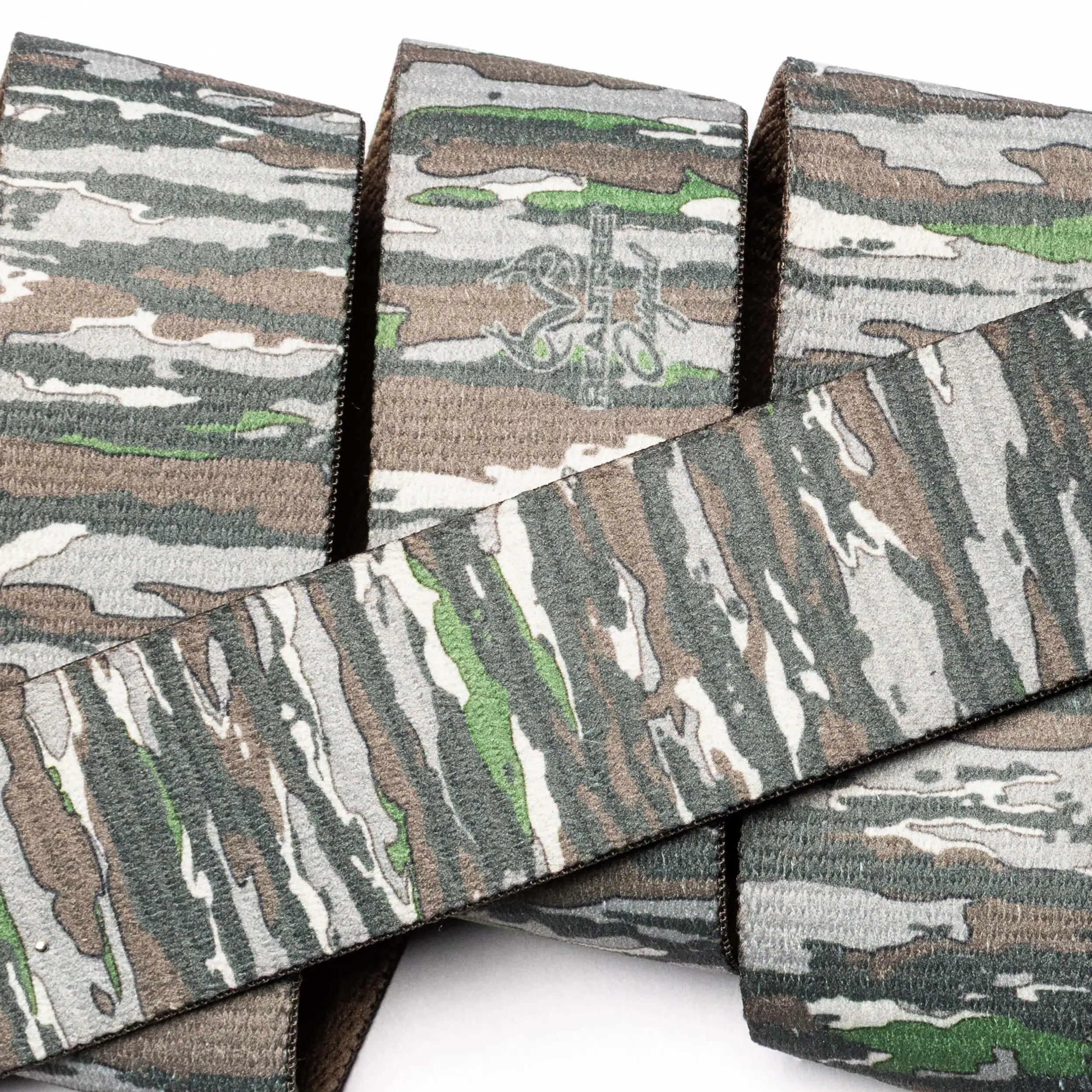 A close-up of Arcade Belts’ Realtree Camo Original, featuring stretch webbing with fabric straps in green, brown, tan, and gray camouflage overlapping against a white background.