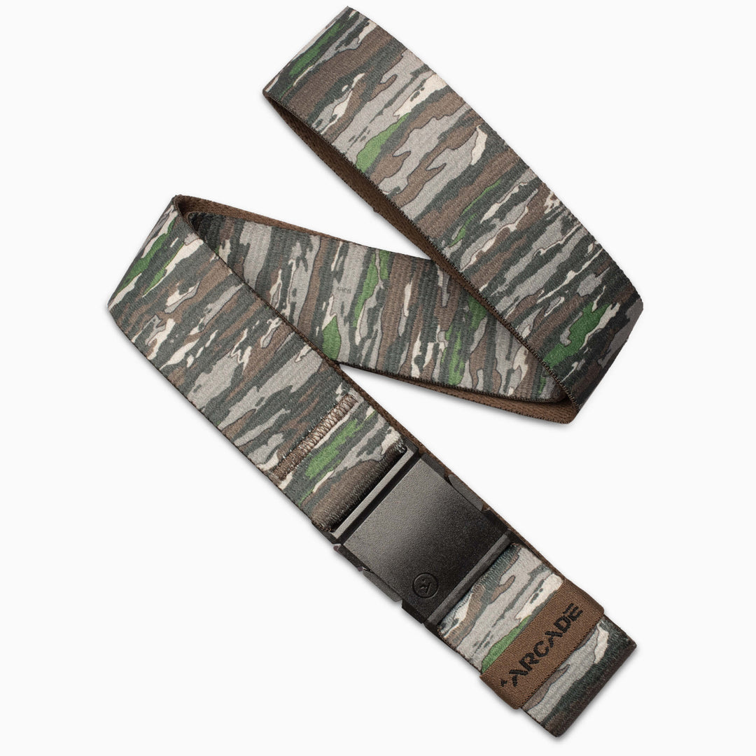 The Arcade Belts Realtree Camo Original is a fabric belt with green, brown, and gray camouflage, a black rectangular buckle, and a tan ARCADE patch. This elastic stretch belt is ideal for travel or daily wear.