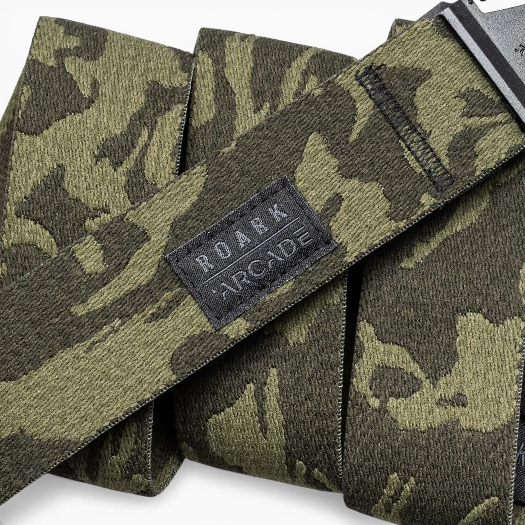 A close-up of green and black camouflage-patterned Roark x Arcade belts by Arcade Belts, featuring a black stitched patch with the ROARK ARCADE logo on one belt.