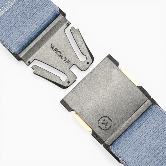Close-up of a metal buckle on a light blue Save the Waves surf belt by Arcade Belts; one side shows the brand name, and the other features a smiley face logo, supporting conservation and Save the Waves initiatives.