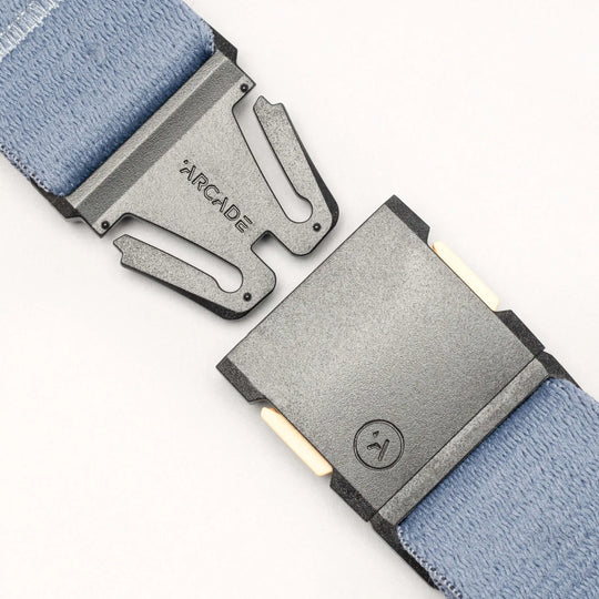 Close-up of a metal buckle on a light blue Save the Waves surf belt by Arcade Belts; one side shows the brand name, and the other features a smiley face logo, supporting conservation and Save the Waves initiatives.