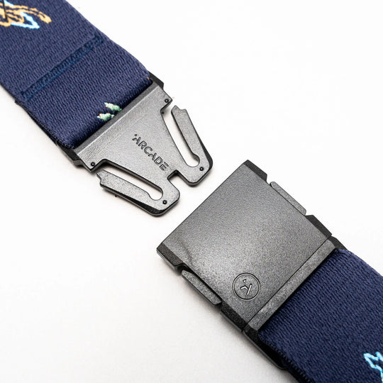 A close-up of the Arcade Belts Save the Waves navy blue stretch belt with a black plastic buckle, partially unfastened. The ARCADE logo is visible on the buckle; perfect for travel belt enthusiasts.