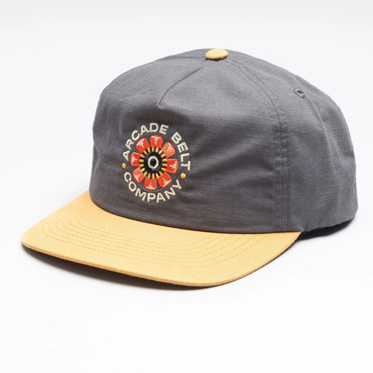 The Arcade Semi Structured Hat by Arcade Belts is a gray cap with a yellow brim and button, showcasing the brand’s logo and a vibrant embroidered design inspired by their iconic Stretch Webbing.