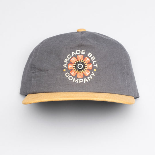 The Arcade Semi Structured Hat by Arcade Belts is a gray cap with a yellow brim and embroidered flower design, plus ARCADE BELT COMPANY on the front—ideal to pair with your favorite low profile belt.