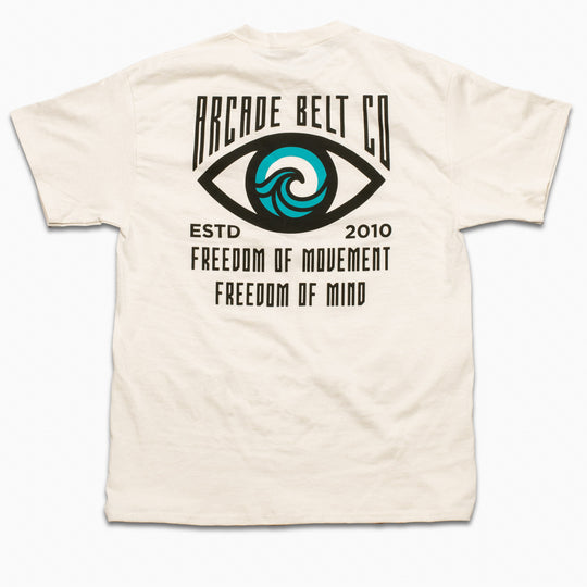 The Arcade Freedom Tee by Arcade Belts is a white T-shirt with an eye design featuring a blue wave in the iris and text: ARCADE BELT CO, ESTD 2010, FREEDOM OF MOVEMENT, FREEDOM OF MIND—celebrating adventure.