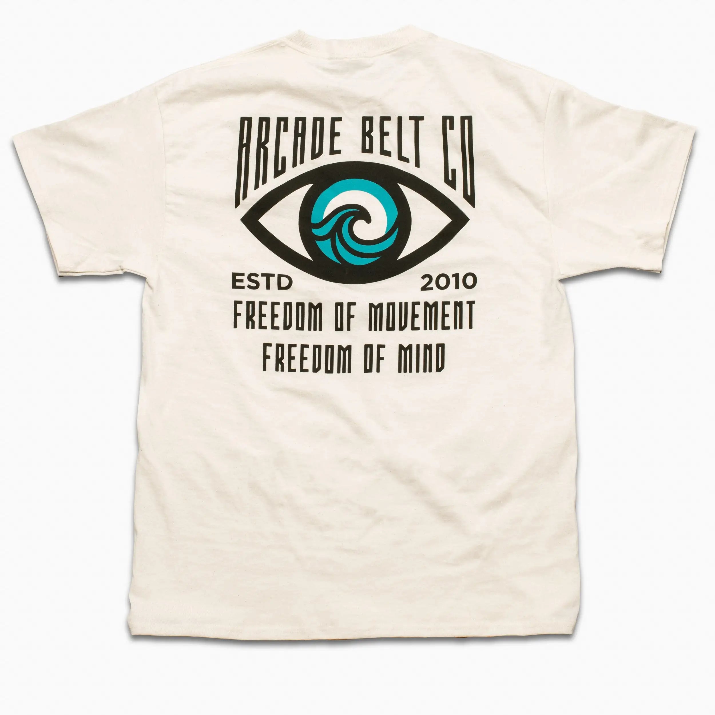The Arcade Freedom Tee by Arcade Belts is a white T-shirt with an eye design featuring a blue wave in the iris and text: ARCADE BELT CO, ESTD 2010, FREEDOM OF MOVEMENT, FREEDOM OF MIND—celebrating adventure.