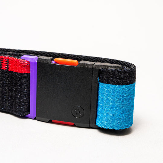 The Sierra by Arcade Belts is a black elastic stretch travel belt with a blue end and a colorful plastic buckle highlighted in orange, red, and purple, shown on a light gray background.