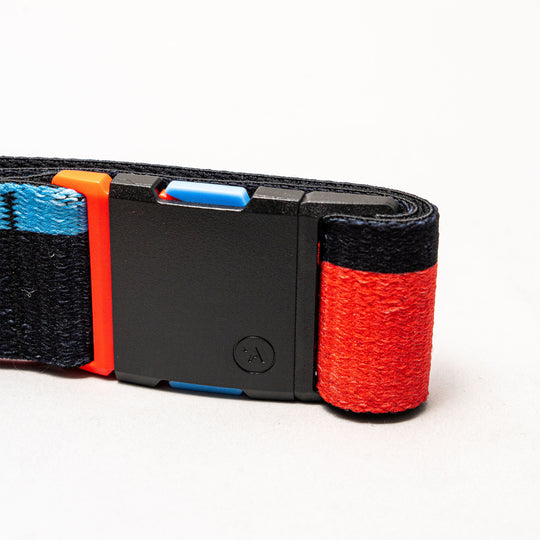 A close-up of the Arcade Belts Sierra, a Stretch Webbing belt with a black plastic buckle. It features blue, red, and orange accents on a dark background, highlighting the brand’s signature vibrant style.