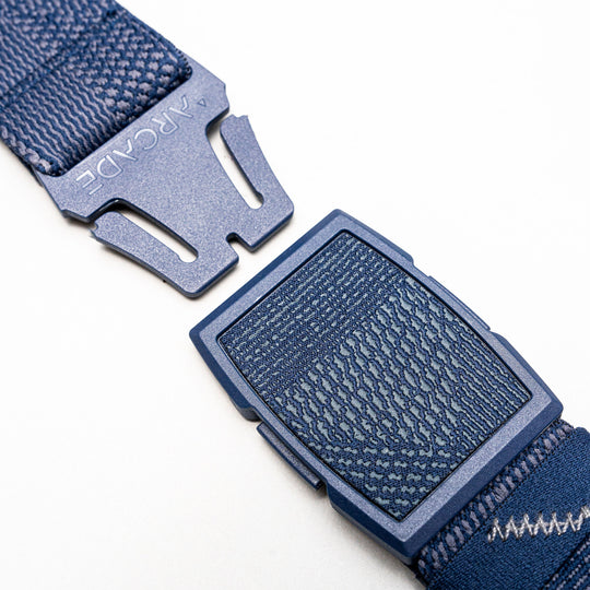 Close-up of the Arcade Belts Skyline, a blue stretch webbing belt with a plastic buckle engraved with “ARCADE,” shown on a plain white background.
