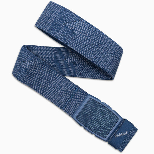 The Skyline belt by Arcade Belts is a blue woven fabric accessory with a geometric pattern, a rectangular blue plastic buckle, and stitched detail at the end—perfectly styled in a loose loop for travel.