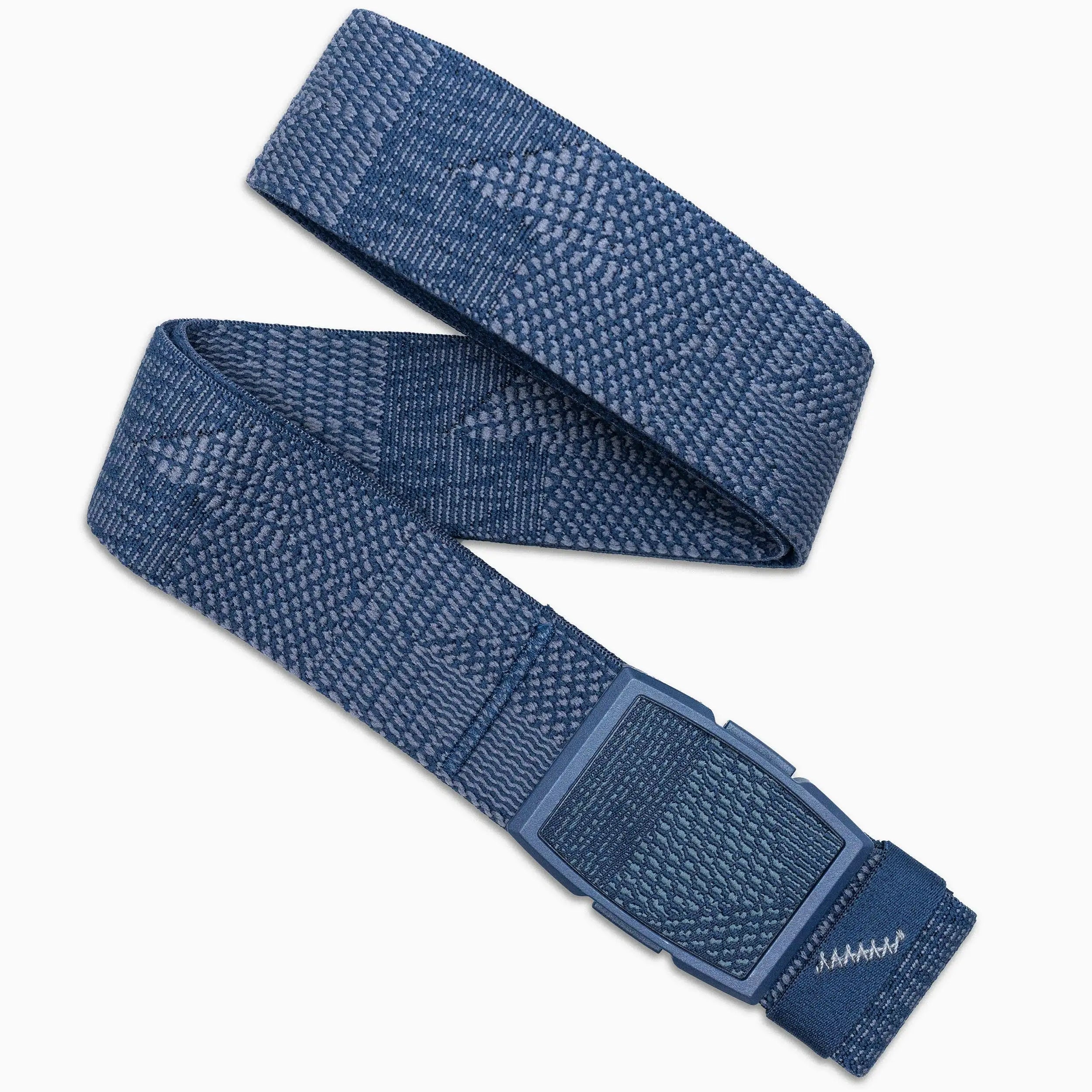 The Skyline belt by Arcade Belts is a blue woven fabric accessory with a geometric pattern, a rectangular blue plastic buckle, and stitched detail at the end—perfectly styled in a loose loop for travel.