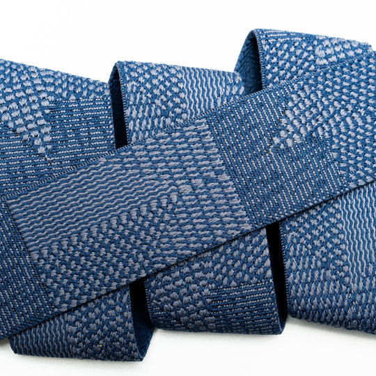 A close-up of a blue woven textile with intricate geometric and wave-like patterns, folded against a white background, reflects the durability and style of the Skyline travel belt by Arcade Belts.