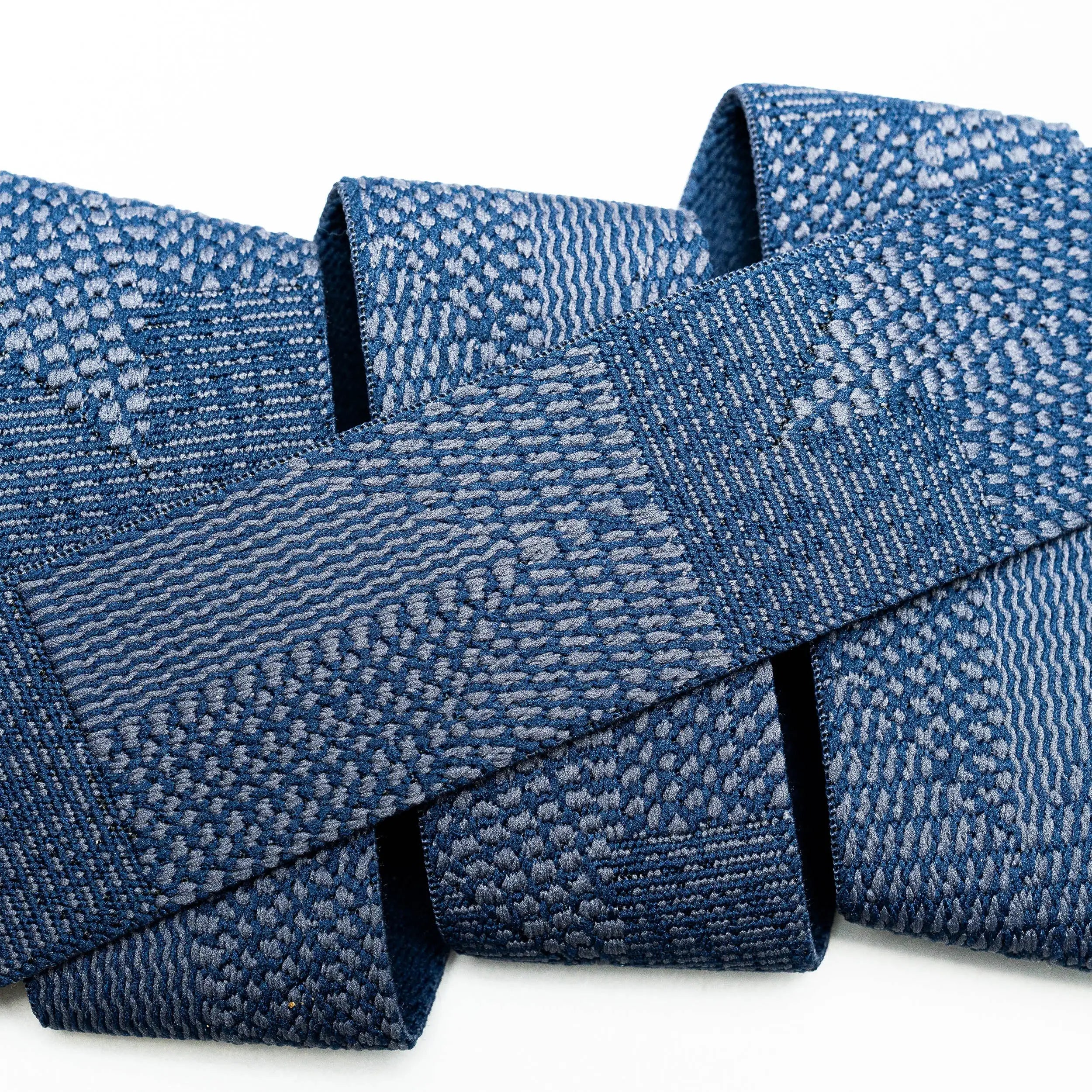 A close-up of a blue woven textile with intricate geometric and wave-like patterns, folded against a white background, reflects the durability and style of the Skyline travel belt by Arcade Belts.