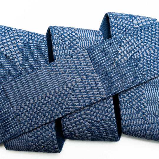 A close-up of a blue woven textile with intricate geometric and wave-like patterns, folded against a white background, reflects the durability and style of the Skyline travel belt by Arcade Belts.