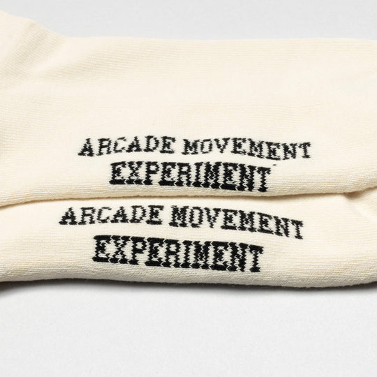 Arcade Movement Experiment Socks by Arcade Belts feature cream color and bold black text—ideal for pairing with Arcade Belts or a low-profile belt on your next adventure.