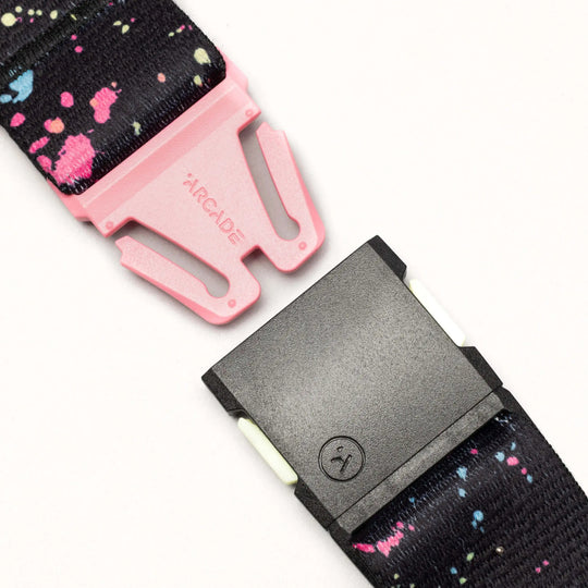 A close-up of the Arcade Belts Splatter: a black belt with vibrant pink and blue drip splatters, a pink ARCADE-labeled buckle, and a black clasp, shown against a light background.
