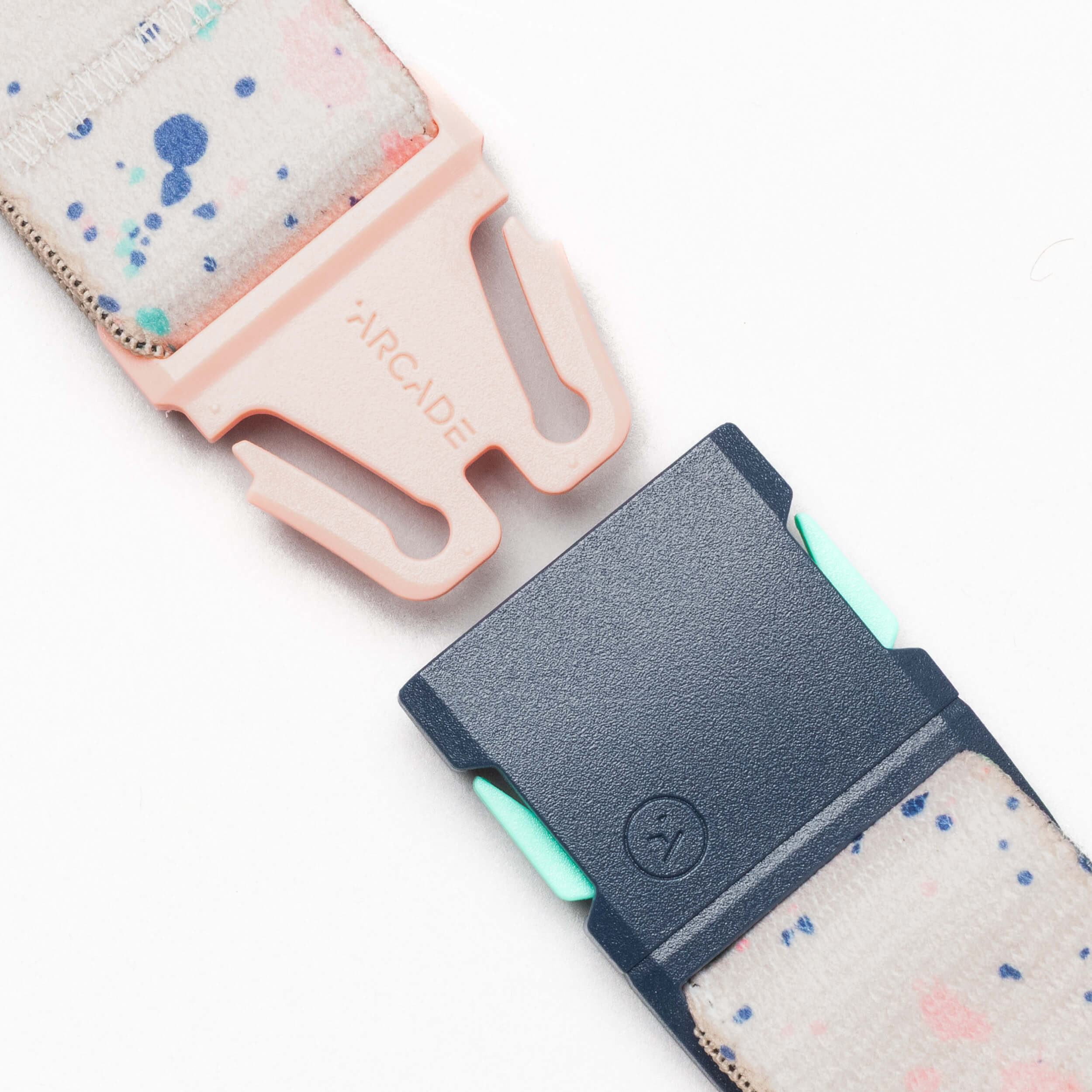 Close-up of the Arcade Belts Splatter: a white strap with colorful splatters, featuring peach and navy buckles labeled ARCADE, shown against a white background.