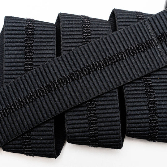 A close-up of the Arcade Belts Stamped black, ribbed elastic band with vertical stitching, neatly rolled on a white surface—perfect stretch webbing for low profile belt designs or use with a plastic buckle.