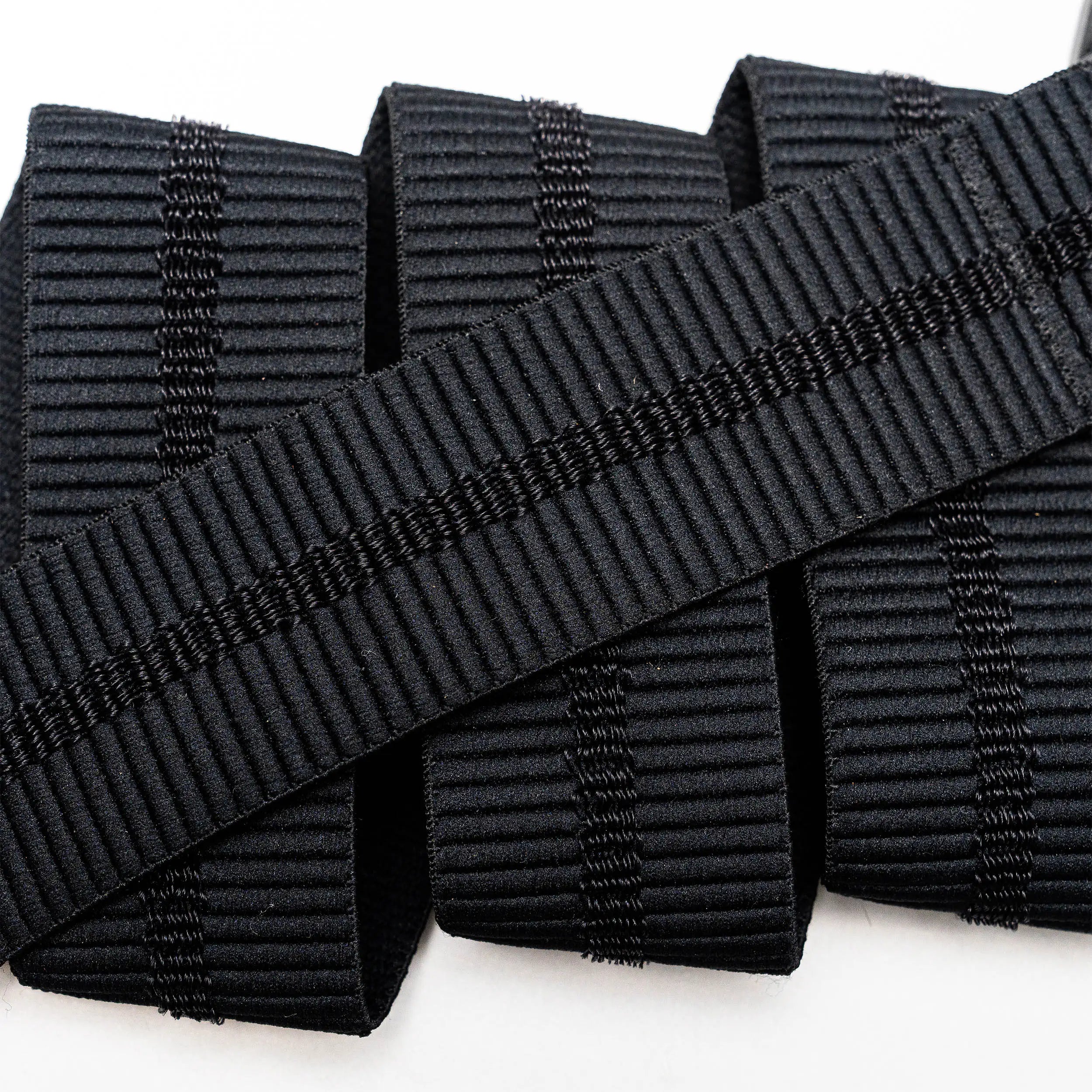 A close-up of the Arcade Belts Stamped black, ribbed elastic band with vertical stitching, neatly rolled on a white surface—perfect stretch webbing for low profile belt designs or use with a plastic buckle.