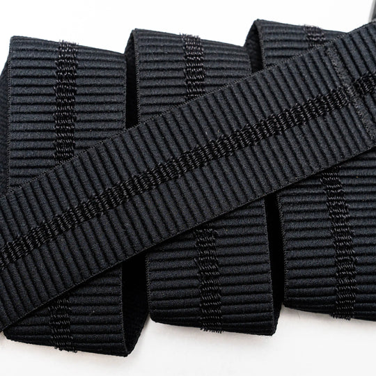 A close-up of the Arcade Belts Stamped black, ribbed elastic band with vertical stitching, neatly rolled on a white surface—perfect stretch webbing for low profile belt designs or use with a plastic buckle.