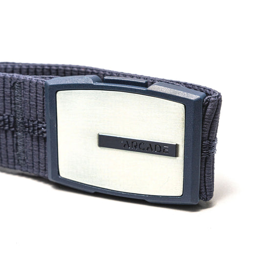 A close-up of the Stamped belt by Arcade Belts, a navy blue elastic stretch belt with a rectangular silver buckle engraved with ARCADE on a small bar across the middle.