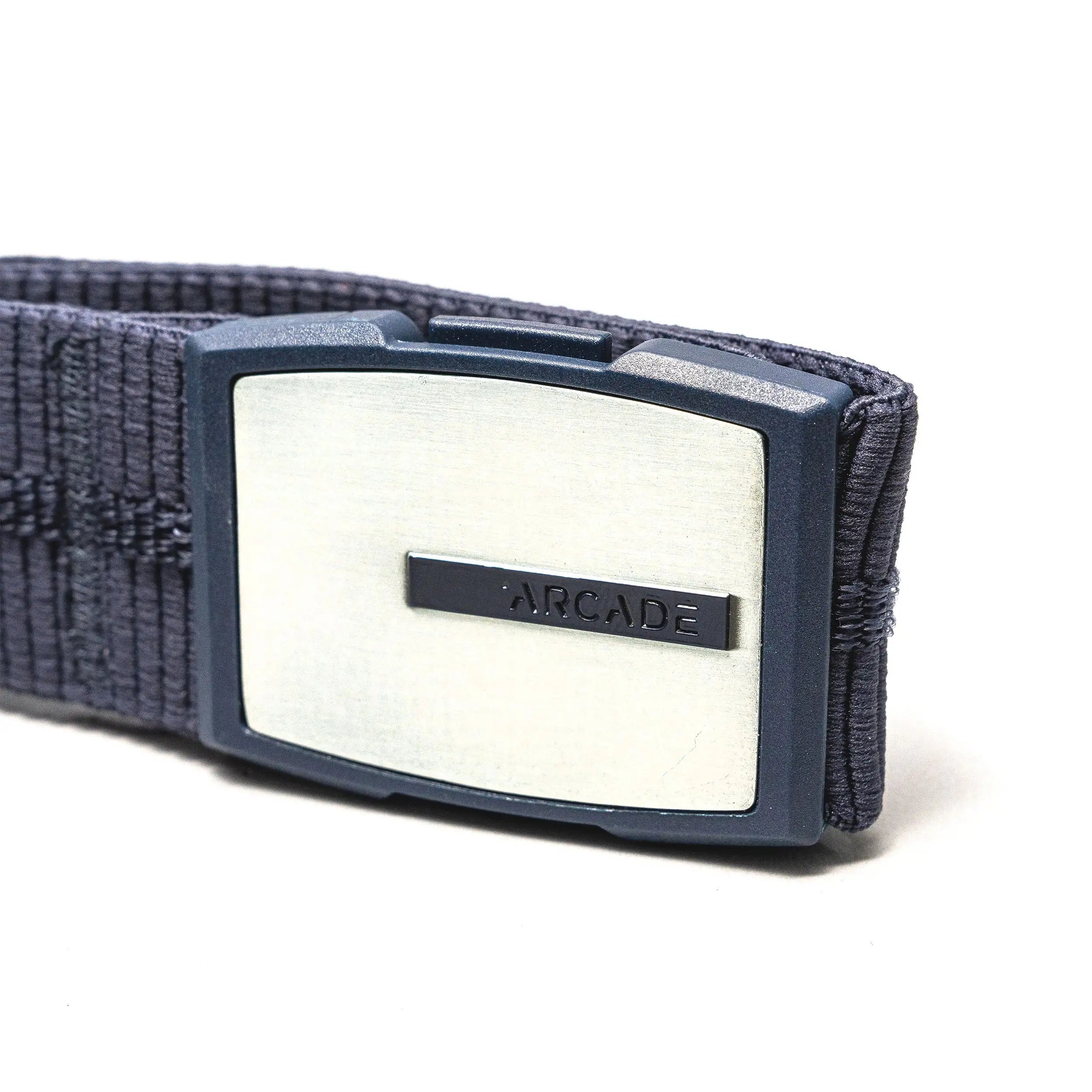 A close-up of the Stamped belt by Arcade Belts, a navy blue elastic stretch belt with a rectangular silver buckle engraved with ARCADE on a small bar across the middle.