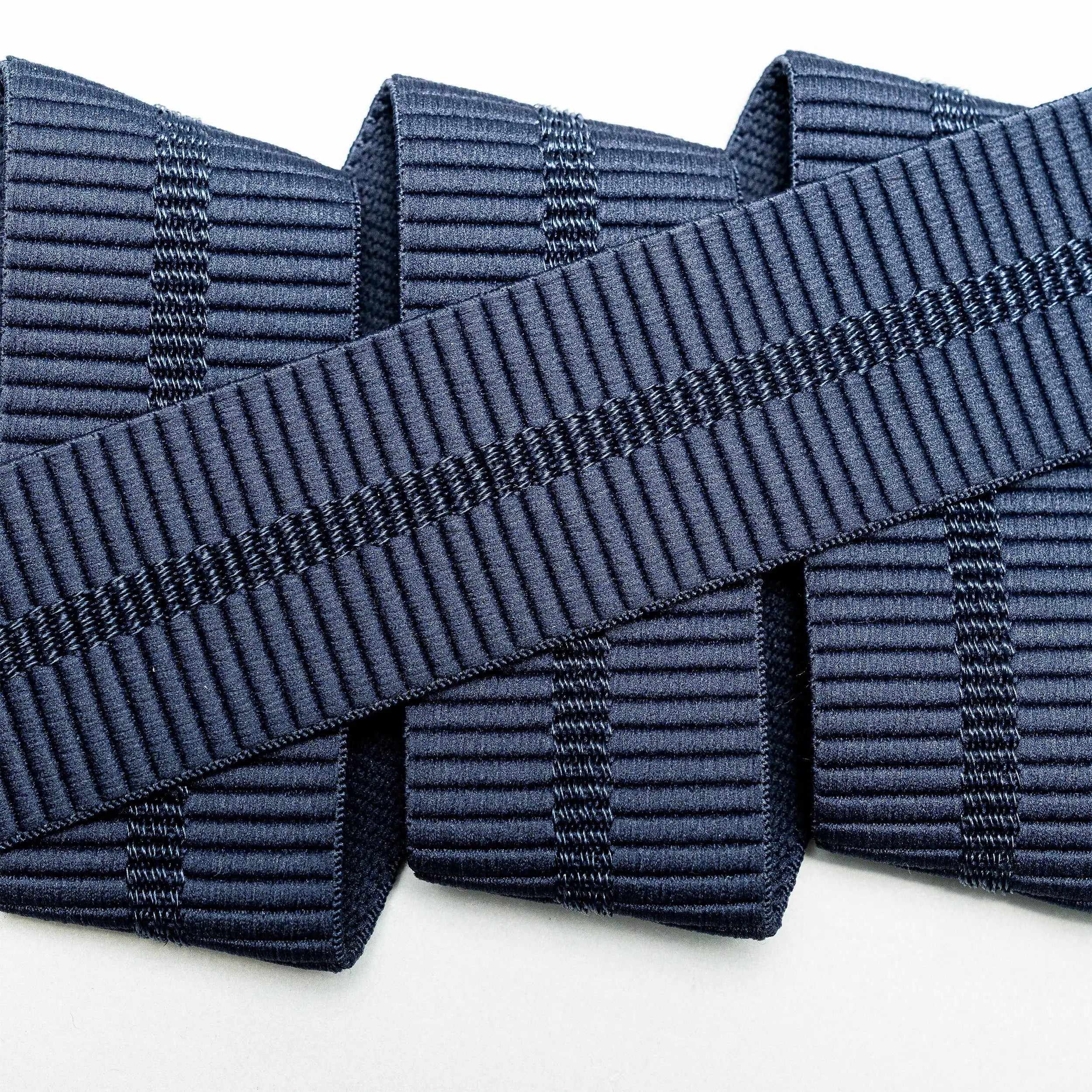 A close-up of three parallel navy blue Stamped stretch webbing ribbons from Arcade Belts, overlapped diagonally by a fourth ribbon with a similar pattern, all set against a white background.