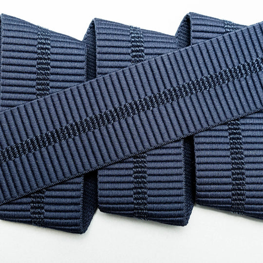 A close-up of three parallel navy blue Stamped stretch webbing ribbons from Arcade Belts, overlapped diagonally by a fourth ribbon with a similar pattern, all set against a white background.