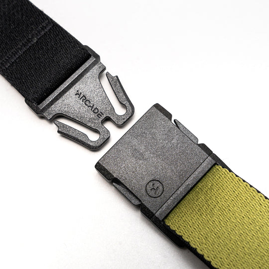 Close-up of the Arcade Belts Static Youth in black and olive green, featuring a metal quick-release buckle engraved with ARCADE, shown unbuckled on a white background.