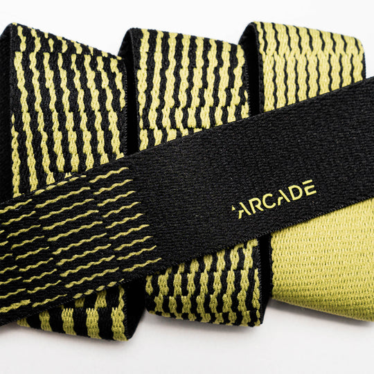 Close-up of the Arcade Belts Static Youth elastic belt, featuring a black and yellow pattern with ARCADE in yellow on a solid black section. Rolled to show its flexibility—ideal for travel.