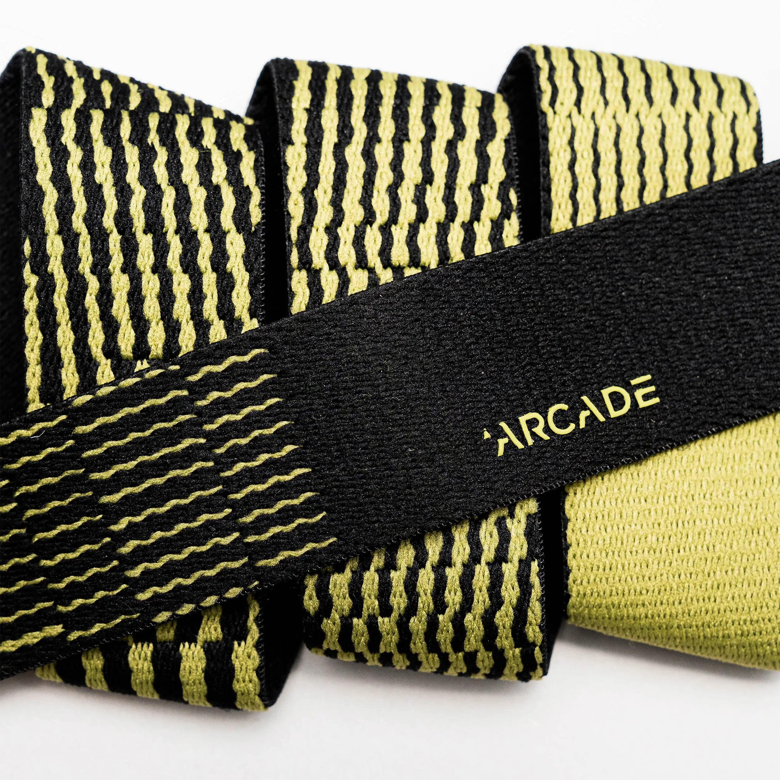 Close-up of the Arcade Belts Static Youth elastic belt, featuring a black and yellow pattern with ARCADE in yellow on a solid black section. Rolled to show its flexibility—ideal for travel.
