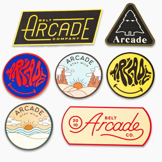 The Arcade Sticker Pack from Arcade Belts features seven vibrant stickers in diverse shapes, showing off nature scenes, bold typography, and playful designs—perfect for personalizing your favorite elastic stretch belt.
