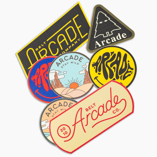 The Arcade Sticker Pack by Arcade Belts features seven colorful stickers with text, abstract graphics, a tree, mountains, sunset, and fun shapes—perfect for pairing with your favorite Plastic Buckle or Elastic Stretch Belt.