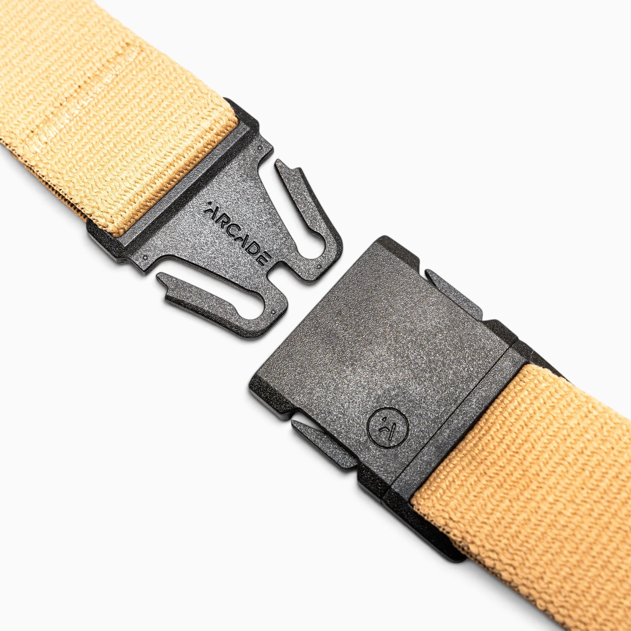 Close-up of the Arcade Belts Treeple tan fabric belt with a black plastic buckle, shown unclasped. The buckle features the word “ARCADE” engraved on one side. Ideal for hanging out with friends or outdoor adventures among trees, this versatile accessory is photographed against a plain white background.
