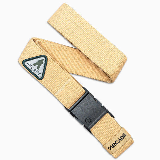 The Arcade Belts Treeple is a beige belt with a black plastic buckle, a small patch of green trees and “ARCADE,” and stitched branding—making it the perfect stylish travel accessory.