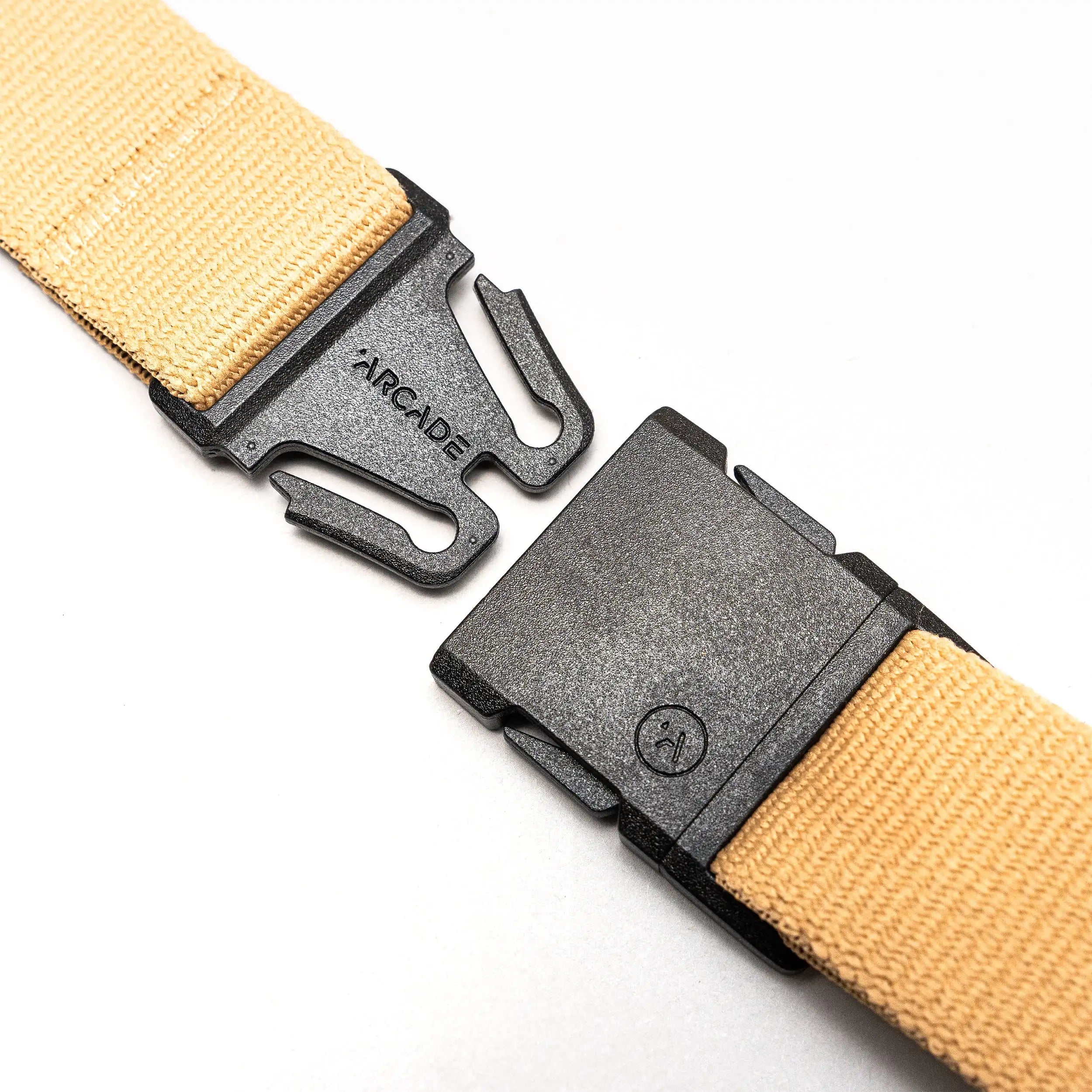 A close-up of the Arcade Belts Treeple beige stretch webbing belt with a black plastic buckle, partially unclasped and displaying the brand name on the male end, set against a white background—ideal for travel.