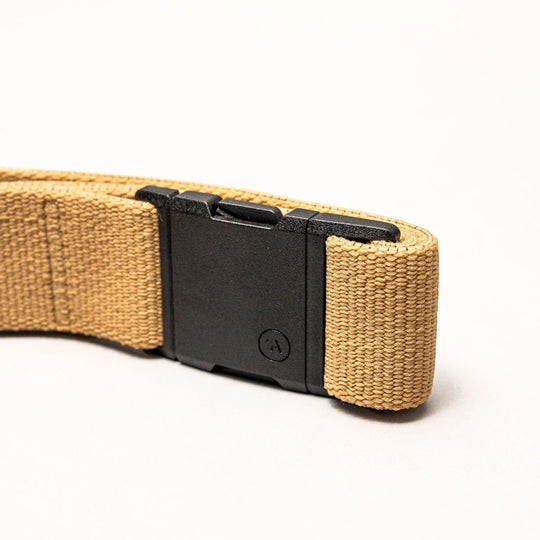 A close-up of the Arcade Belts Treeple, a tan woven elastic stretch belt featuring a black rectangular plastic buckle, ideal as a low-profile travel belt, shown against a plain white background.