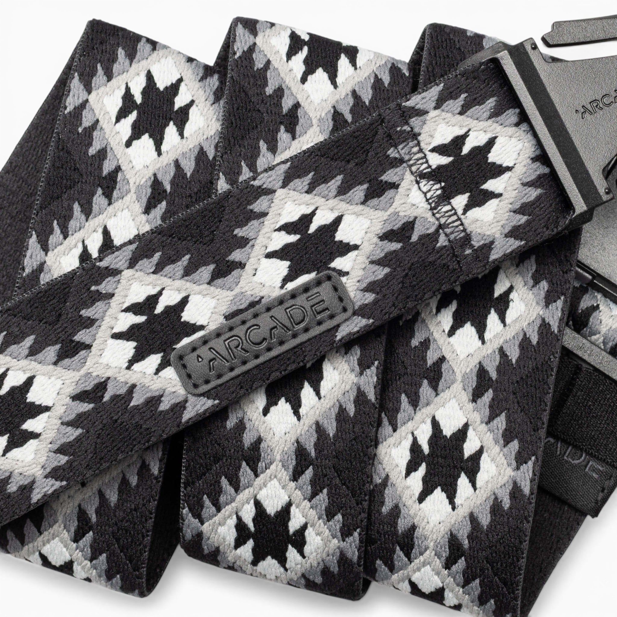 A close-up of the Vernan Kee belt by Arcade Belts, showcasing its black, white, and gray geometric pattern inspired by Navajo rug designs, with a black plastic buckle and a stitched Arcade label.