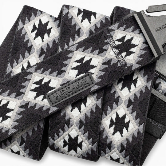 A close-up of the Vernan Kee belt by Arcade Belts, showcasing its black, white, and gray geometric pattern inspired by Navajo rug designs, with a black plastic buckle and a stitched Arcade label.