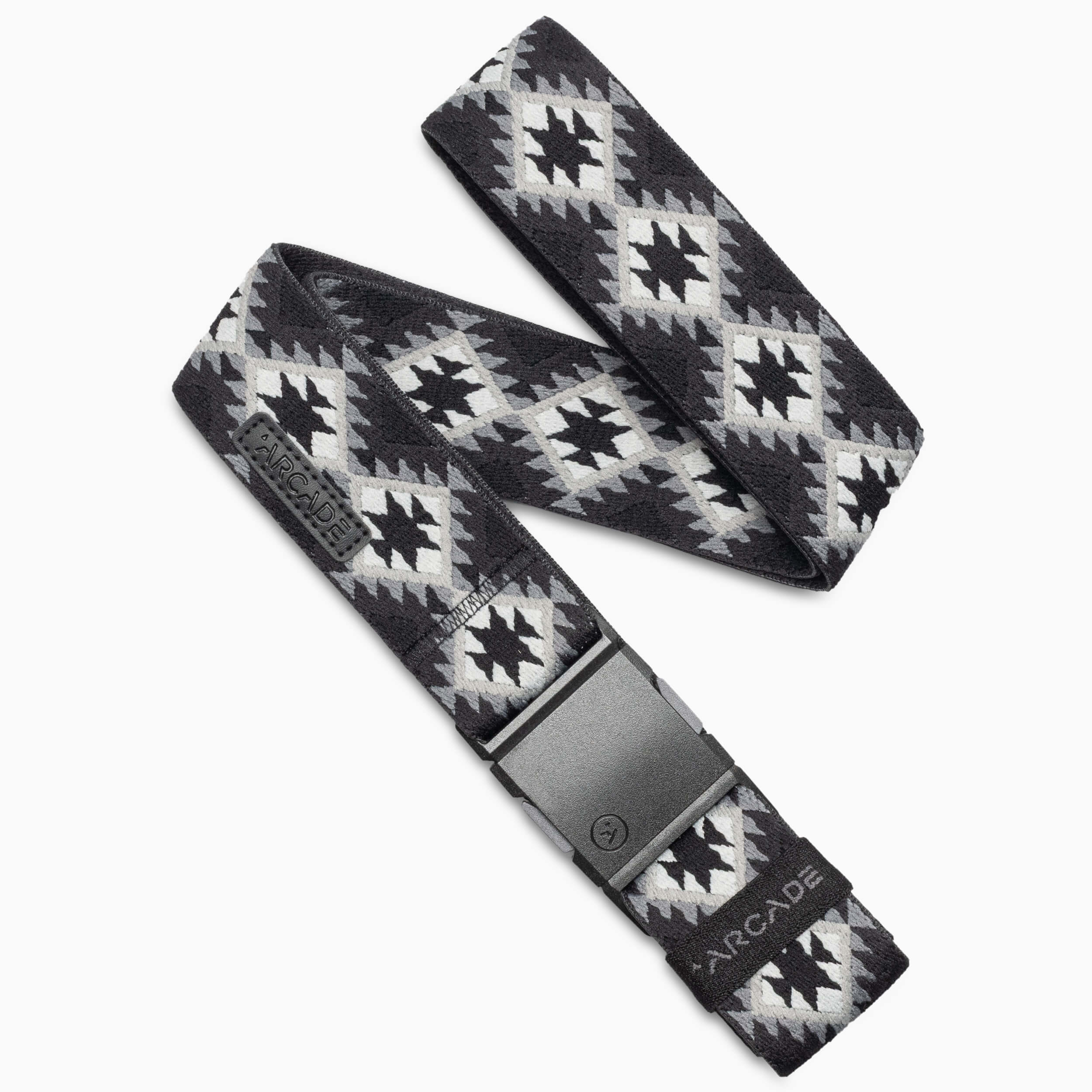 A black and grey Arcade Belts Vernan Kee fabric belt featuring geometric patterns inspired by traditional rugs, with a black plastic buckle and the Arcade brand name displayed near the buckle.