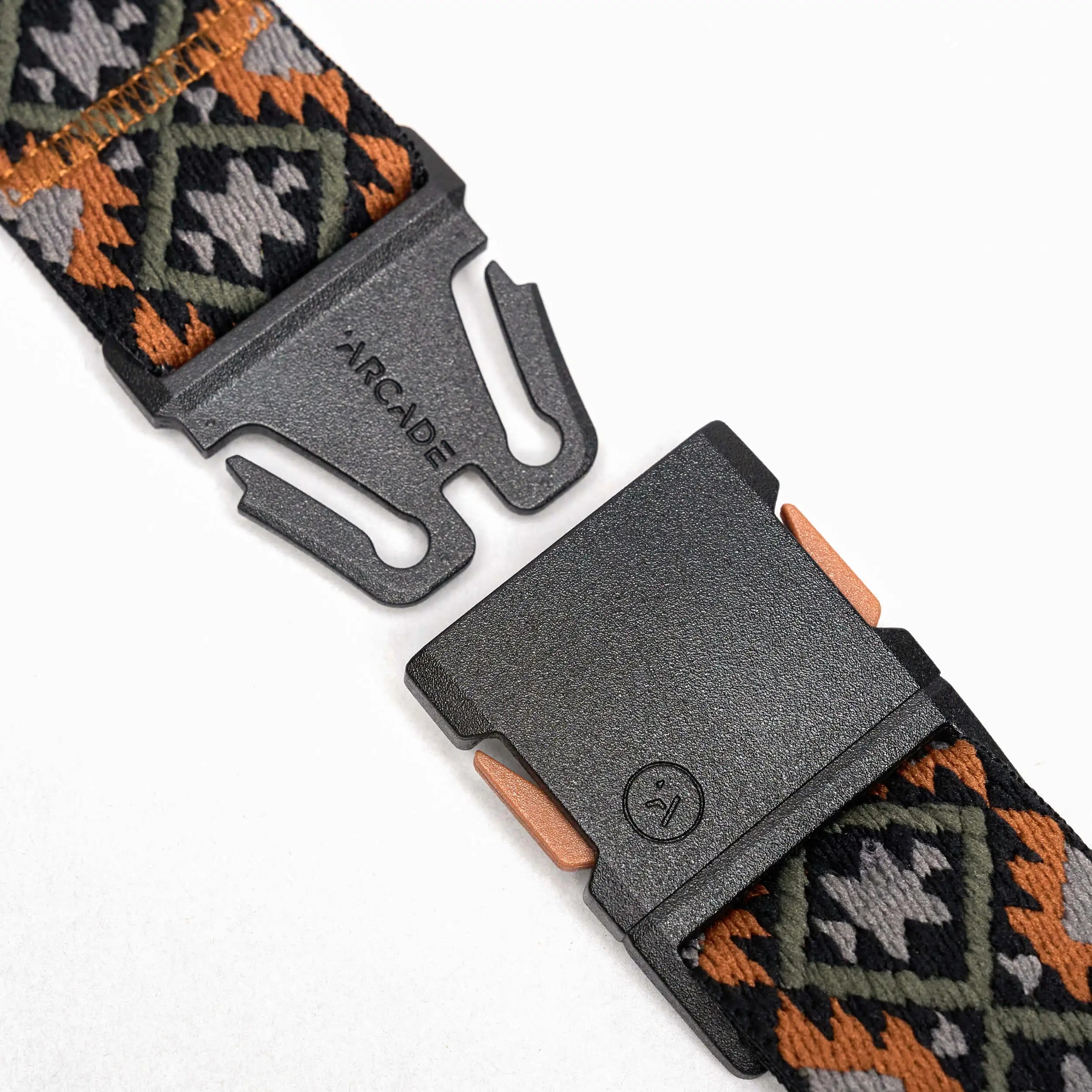 Close-up of Arcade Belts Vernan Kee travel belt with an unfastened black plastic buckle. Features stretch webbing with a geometric black, orange, and green design. ARCADE branding is visible on the buckle.