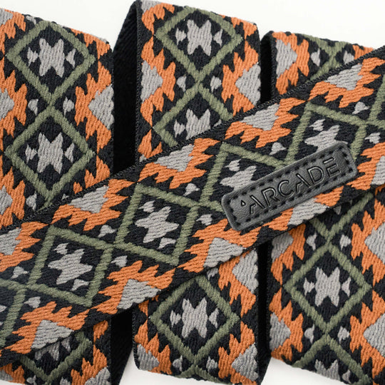 A close-up of woven fabric with a geometric pattern in orange, dark green, black, and gray. A black label displays the word ARCADE on a strap, highlighting Arcade Belts’ Vernan Kee design.
