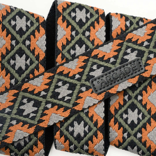 A close-up of woven fabric with a geometric pattern in orange, dark green, black, and gray. A black label displays the word ARCADE on a strap, highlighting Arcade Belts’ Vernan Kee design.