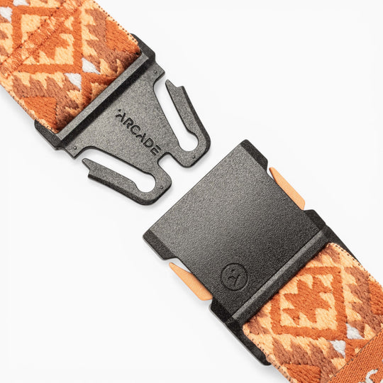 A close-up of the Vernan Kee belt by Arcade Belts showcases its patterned brown fabric with traditional rug-inspired designs and a black plastic buckle labeled ARCADE, displayed partially unclasped against a white background.