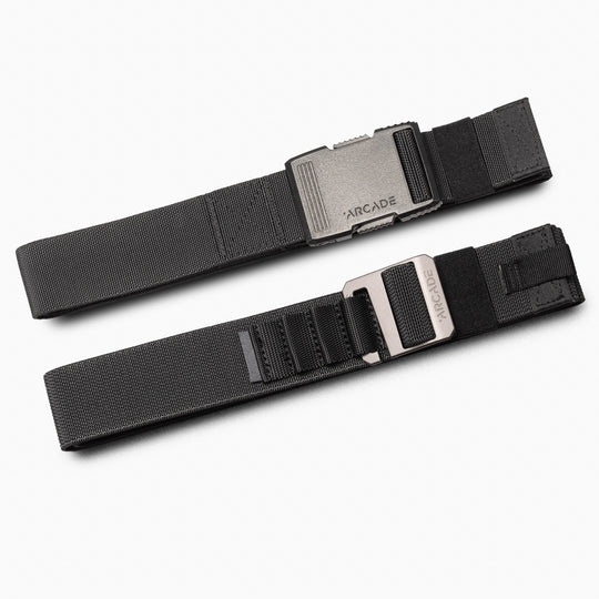 Two black Utility Long Kit belts from Arcade Belts, featuring adjustable elastic webbing and engraved metal buckles, are placed parallel on a white background. Webbing loops near the clasps complete the design.