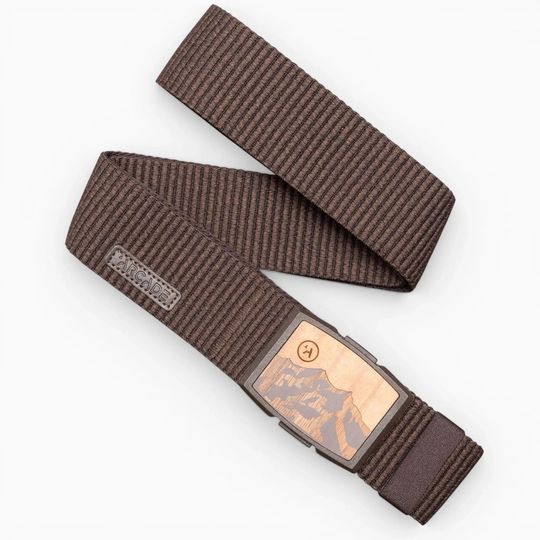 The Woody belt by Arcade Belts is a brown striped stretch belt with a rectangular metal buckle featuring a mountain design and an engraved logo tag near the buckle, shown laid out in a zigzag pattern on a white background.