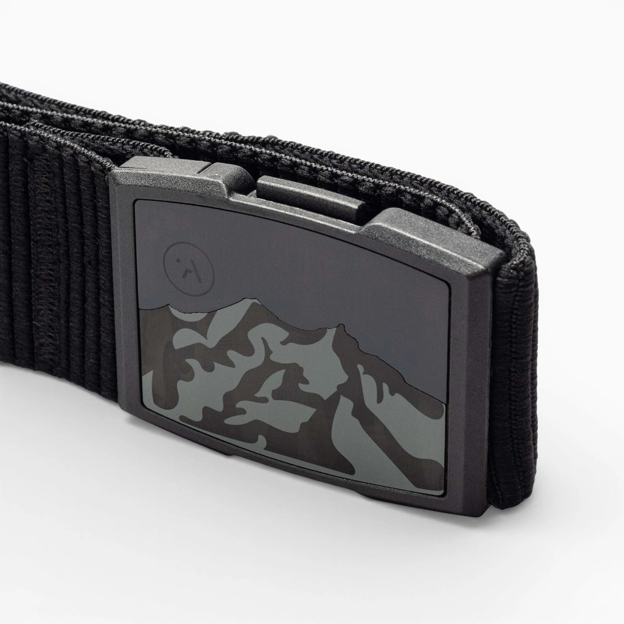 Close-up of the Arcade Belts Woody elastic stretch belt with a metal buckle featuring a mountain range design and an etched moon or sun in the corner. The white background highlights this low-profile belt.